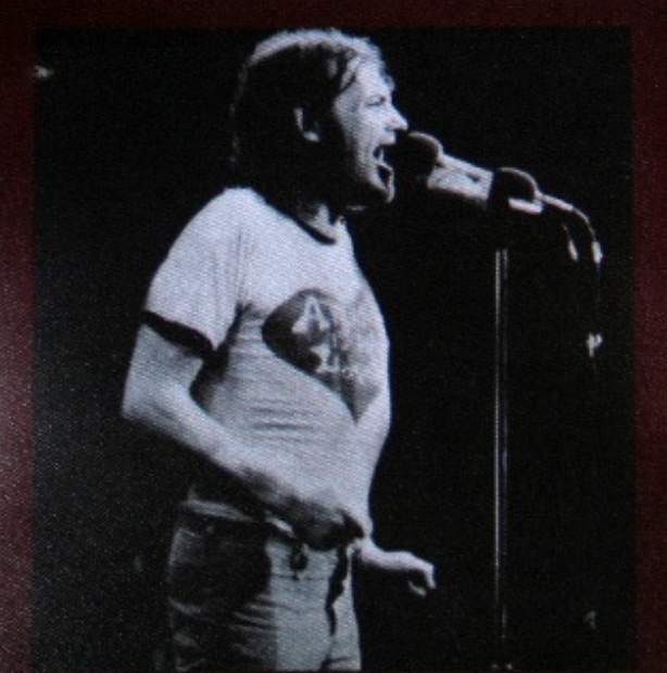 A black and white photograph of a man singing into a microphone on stage.