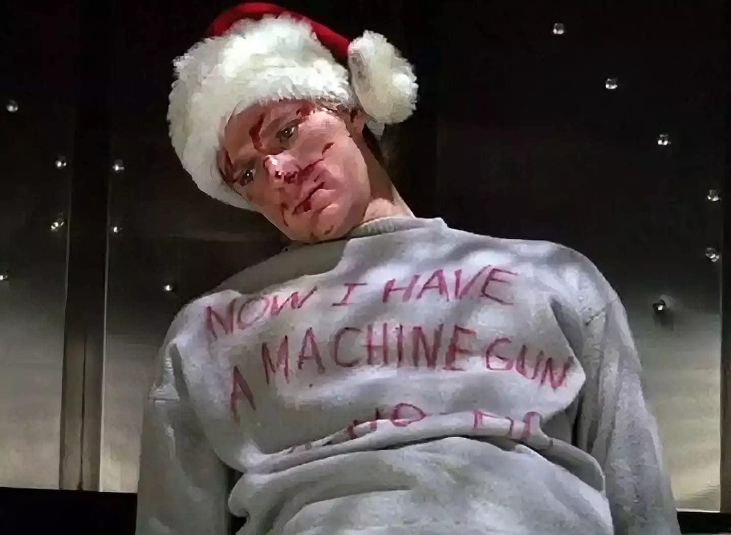 A person wearing a Santa hat and a gray sweatshirt with the text "Now I have a machine gun" written on it.