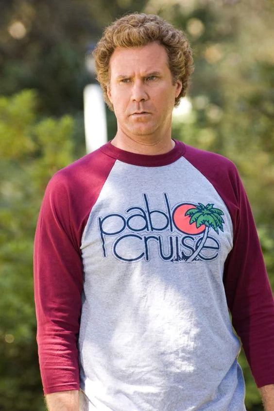 A man wearing a red and gray shirt with the text "Pablo Cruise" on it, standing outdoors in a natural setting.