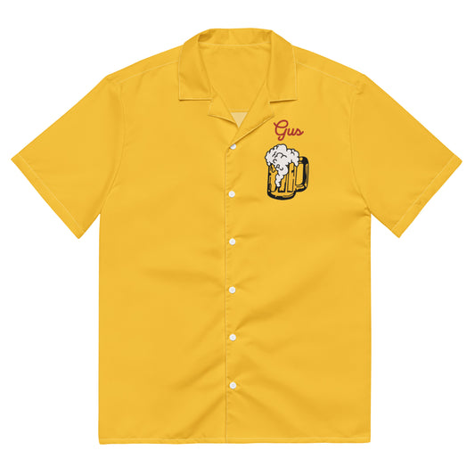 The front of a vintage mustard yellow button up costume shirt that says "Gus". Image of beer foaming out of a tankard. Worn by actor John Candy and character Gus Polinski in the movie "Home Alone".