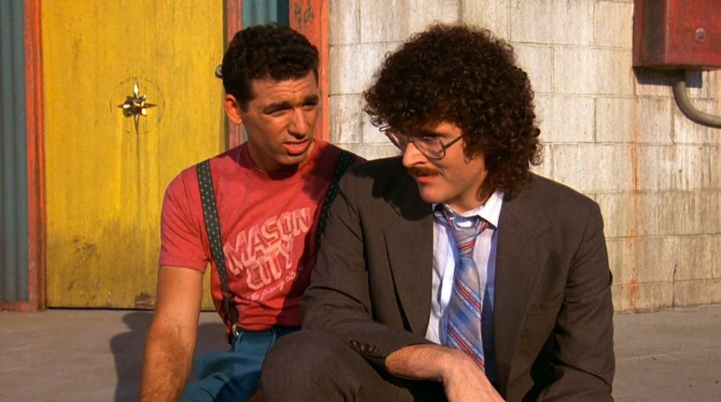 two men sitting next to each other in front of a building