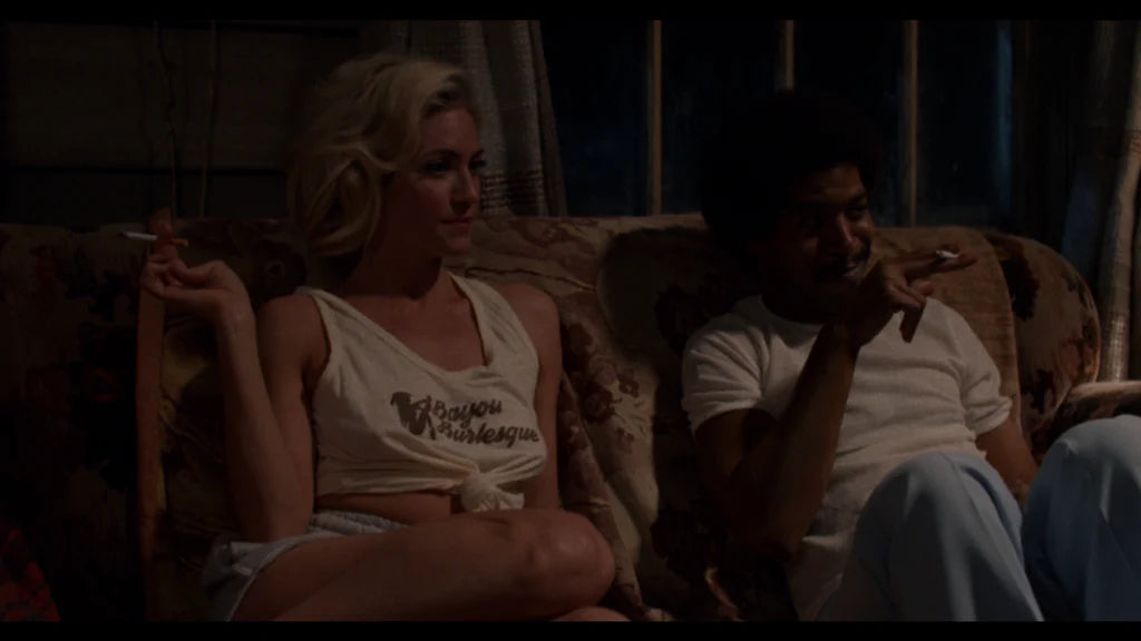 a woman and a man sitting on a couch, both holding cigarettes and appearing to be in a relaxed, intimate setting.