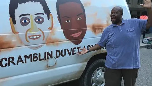 A man is standing next to a white van with a drawing of two faces on it.