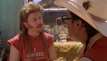 two men engaged in a conversation, with one man wearing a red t-shirt with the text "I CHOKED Linda Lovelace" and the other wearing a large cowboy hat.