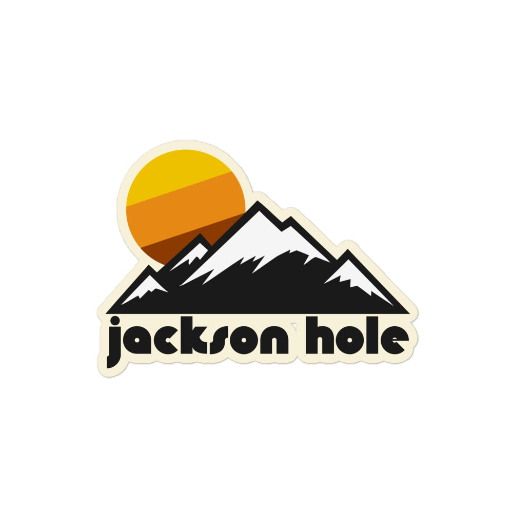 A retro, vintage Jackson Hole kiss cut sticker with the image of a mountain range with snow and a yellow, orange, and reddish brown sun rising behind, referencing the town and mountain resort in Grand Teton National Park.
