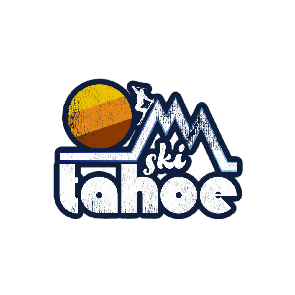 A vintage "Ski Tahoe" kiss cut sticker including a skier headed down mountain peaks in a stylized fashion next to a huge, aesthetic yellow, orange, and brown sun. Lake Tahoe, bordering California and Nevada, is known for its many ski resorts, including Palisades Tahoe.