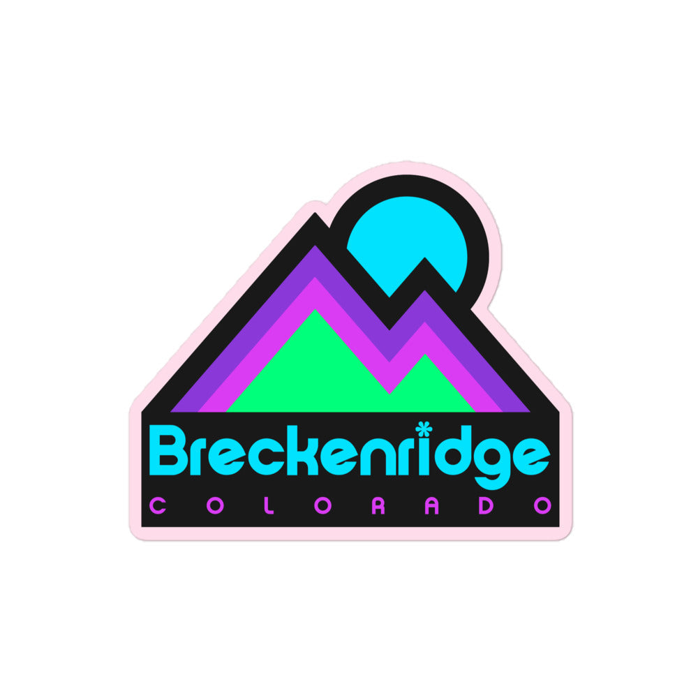 A retro Breckenridge Colorado kiss cut sticker in electric blue, purple, pink, and mint green colors. Includes image of a mountain range and rising sun in reference to the town and ski resort in the Colorado Rocky Mountains.