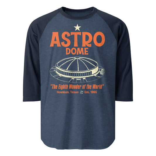 A heather and navy blue vintage 3/4 sleeve raglan style shirt that says "Astro Dome" from "Houston, Texas" which was established in 1965 as the first domed stadium in the world. Coined as "The Eighth Wonder of the World" by Judge Roy Hofheinz. Shirt has the image of the circular baseball stadium with a domed ceiling and a small baseball which served the Houston Astros MLB team and the Houston Oilers NFL team.