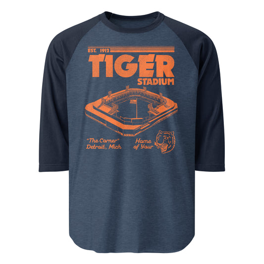 A heather blue and navy vintage 3/4 sleeve raglan style shirt for the Tiger Stadium, Established in 1912, nicknamed "The Corner" due to being at the intersection of Trumbull and Michigan Avenues. Says "Home of Your Tigers" with an image of a tiger in orange, referencing the Detroit Tigers MLB team. The Detroit Lions NFL team also played in the stadium.
