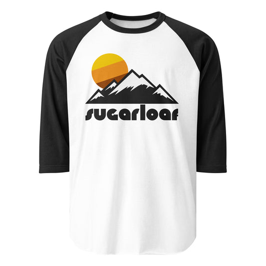 A white and black 3/4 sleeve raglan retro style shirt that says "Sugarloaf" - referencing the mountain and ski resort in Maine - underneath the image of a couple mountains, covered in snow, under a setting sun.