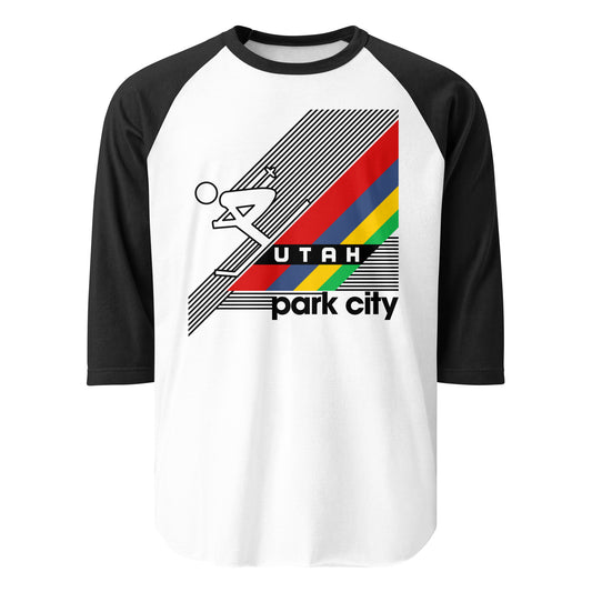 A black and white 3/4 sleeve raglan style shirt for tourists that says Park City, Utah. Image of red, blue, yellow, and green stripes serving as a mountain slope and person skiing downhill. References the Park City Mountain Resort and the Wasatch Mountain range.