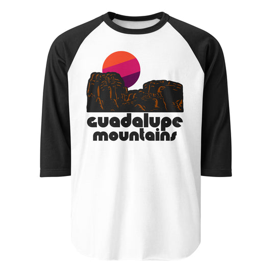 A black and white retro raglan style three quarter sleeve shirt. Says "Guadalupe Mountains." Has image of red rock mountain landscape in front of a rising sun.