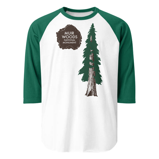 A three quarter sleeve retro raglan style kelly green and white shirt that says Muir Woods National Monument on top of a brown paw print, next to a tall green and brown famous redwood tree. The forest is named for naturalist and conservationist John Muir, and is located in California and the homelands of the Coast Miwok people.