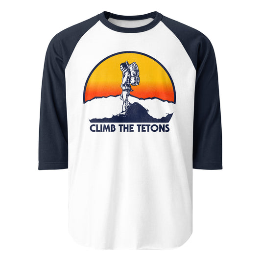 A 3/4 sleeve white and navy raglan shirt for Grand Tetons tourists. Text reads "Climb The Tetons", referencing the Grand Teton National Park, most famous for its tallest peak, Grand Teton, in northwest Wyoming. Image of a hiker traversing the top of a cliff, backpacking gear on, as a sun sets in orange and yellow colors.