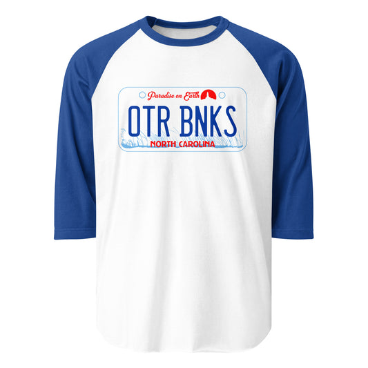 A royal blue and white 3/4 sleeve raglan retro style t-shirt with a license plate that reads OTR BNKS, North Carolina, Paradise on Earth. Image of blue American beachgrass and a small red lighthouse icon. References Netflix mystery and drama TV series "Outer Banks, starring Chase Stokes, Madelyn Cline, Rudy Pankow, Madison Bailey, Jonathan Daviss, and Drew Starkey.