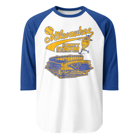 A 3/4 sleeve royal blue and white raglan 80s style Milwaukee County Stadium t-shirt. Image of a yellow and blue baseball player wearing a "Brew Crew" jersey hitting a baseball with a bat over the stadium, later replaced by Miller Park and the American Family Field.