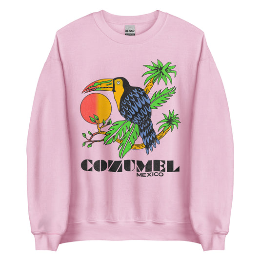 A light pink Cozumel Mexico crew neck sweatshirt that has a tropical bird with blue feathers sitting on island palm trees in front of a red orange sunrise. Refers to the cruise ship resort destination in the Caribbean Sea.