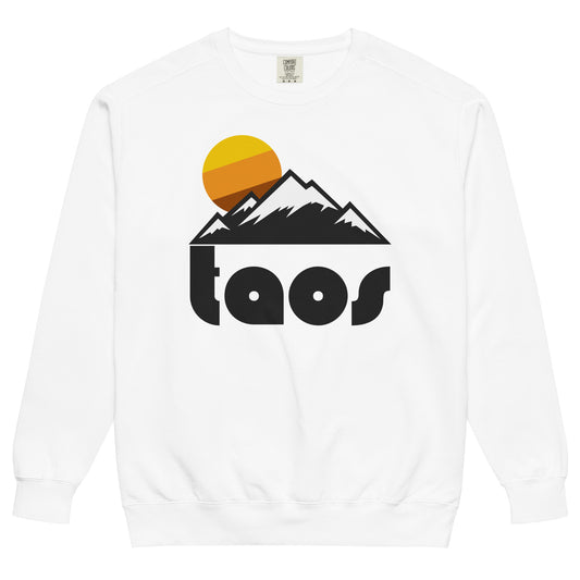 A tourist, retro white crew neck sweatshirt with the word "taos" in black letters referencing Taos Ski Valley, New Mexico, a world famous southwestern ski resort in the Sangre de Cristo Mountain Range, the southernmost part of the Rocky Mountains, near the Rio Grande and the Rio Grande Gorge. The sweatshirt includes a picture of multiple mountain peaks covered in snow and a striped yellow/orange/brown sun rising in the distance.