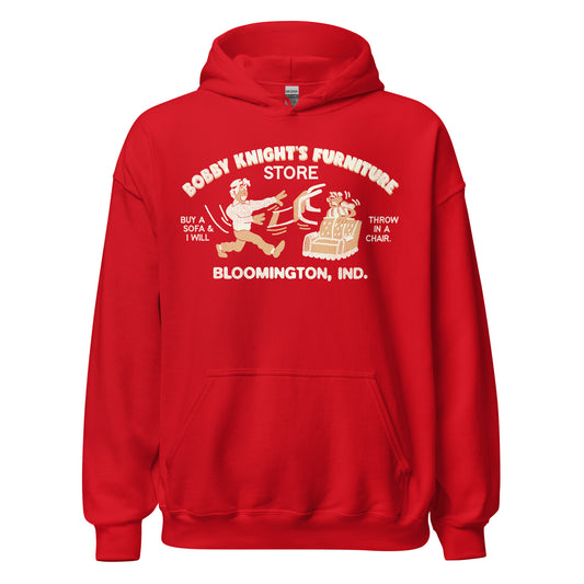 A bright red travel hooded sweatshirt that says "Bobby Knight's Furniture Store". Has the image of a furniture salesperson throwing a chair at a customer ducking behind a couch with the silly pun "Buy a sofa & I will throw throw in a chair". Shirt from "Bloomington, Ind."