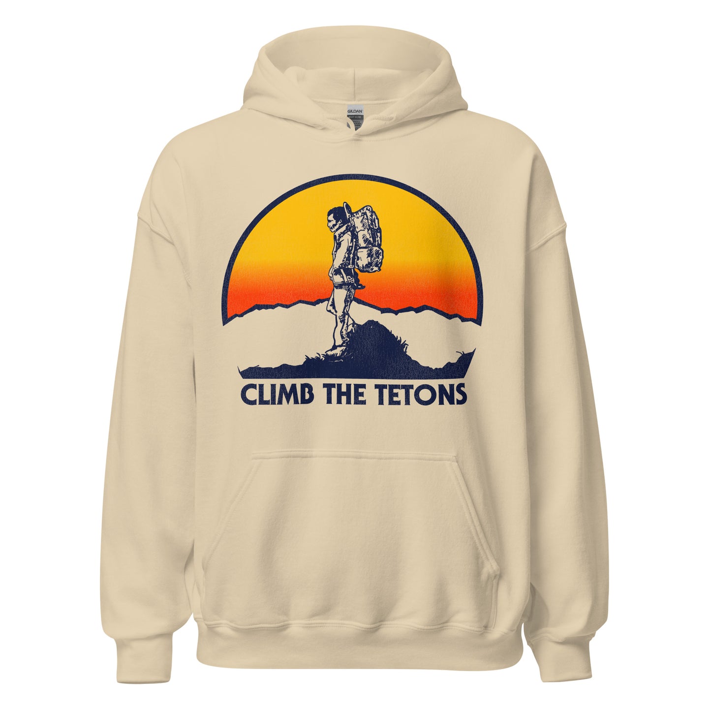 A sand colored 80s style tourist hoodie sweatshirt with a hiker at the top of a mountain, hands in pockets, as a huge sun sets. Words say "Climb the Tetons", referencing the famous national park The Grand Tetons, located near Jackson, Wyoming and Yellowstone National Park.