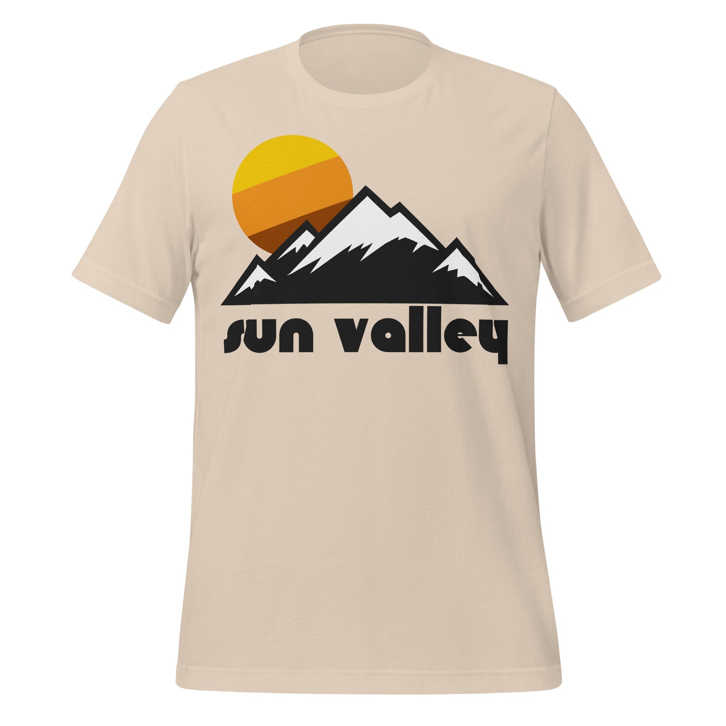 A soft cream souvenir t-shirt that says "Sun Valley", referencing Sun Valley Resort in the Smoky Mountains and Pioneer Mountains of Idaho, in the greater Rocky Mountains area, known for its incredible skiing hills. Shirt includes image of a mountain landscape with snowcapped peaks and a tricolored sun setting in the background.