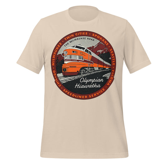 A soft cream colored retro 70s style t-shirt that says "The Milwaukee Road", a network of railroads that connected American cities Chicago, Milwaukee, the Twin Cities, Spokane, Seattle, and Tacoma. Image of an Olympian Hiawatha Speedliner Service orange, red, and white train that is labeled "Milwaukee Road" in front of red mountains and dark forests.