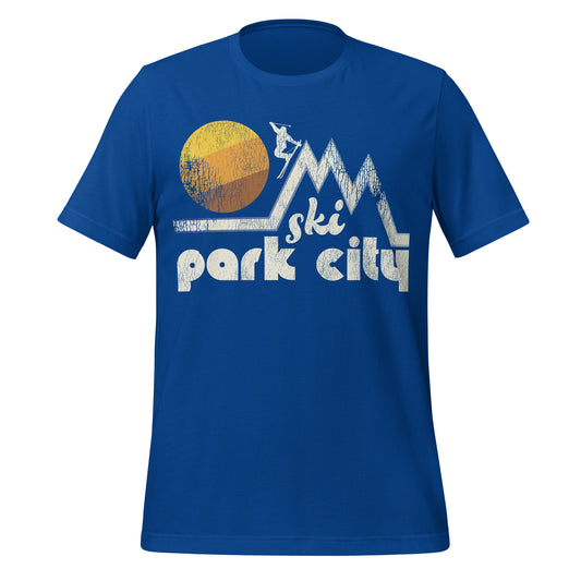 A royal blue colored "Ski Park City" vintage t-shirt with the image of a person skiing down one of multiple triangular mountains, a striped warm toned sun in the background. Park City, Utah, is known for the stunning Wasatch Mountains and famous ski resorts Deer Valley Resort and Park City Mountain Resort.