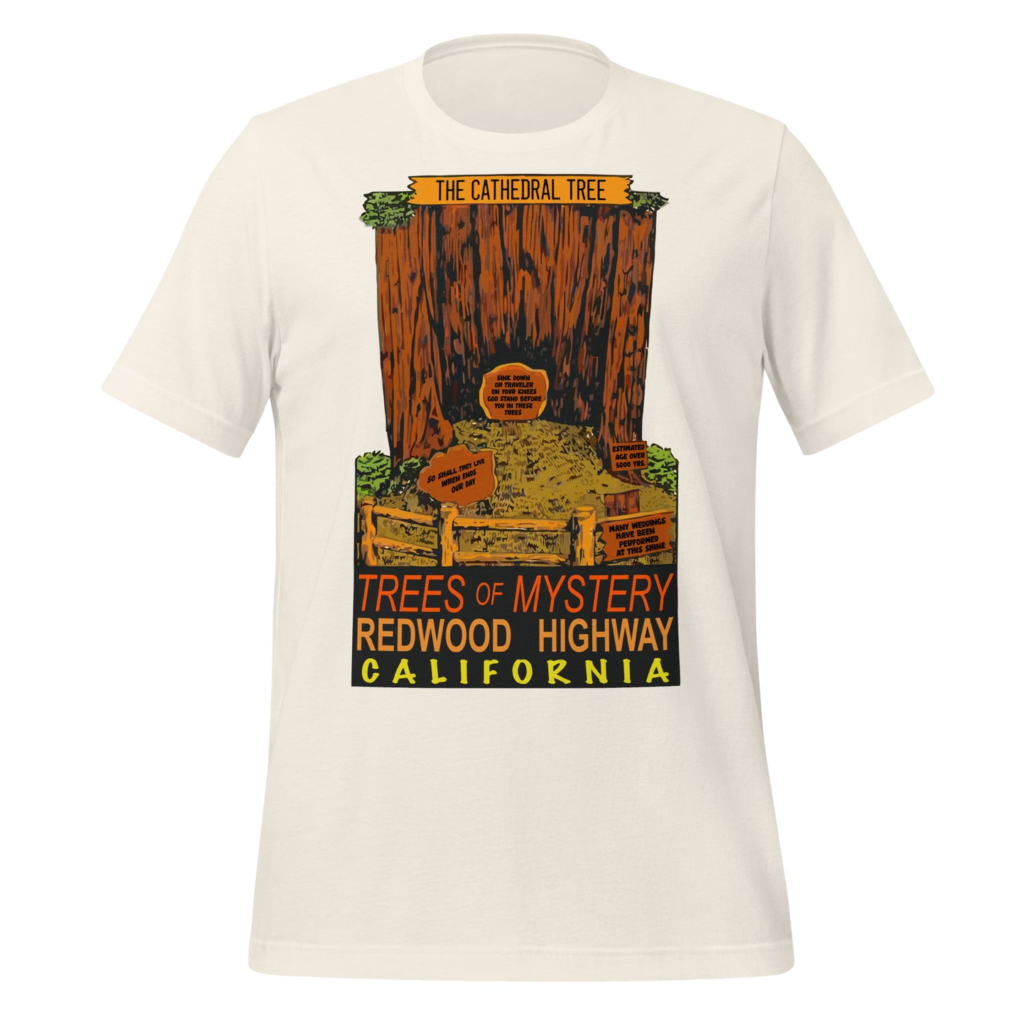 A retro vintage white colored t-shirt with an image of "The Cathedral Tree", a hollowed out redwood surrounded by wooden fences and historical signs saying "Estimated Age Over 500 Years", "So Shall They Live When Ends Our Day", "Sink Down, Oh Traveler, On Your Knees, God Stand Before You In These Trees", and "Many Weddings Have Been Performed At This Site". T-shirt also says "Trees of Mystery", "Redwood Highway", and "California" in red, orange, and yellow colors.