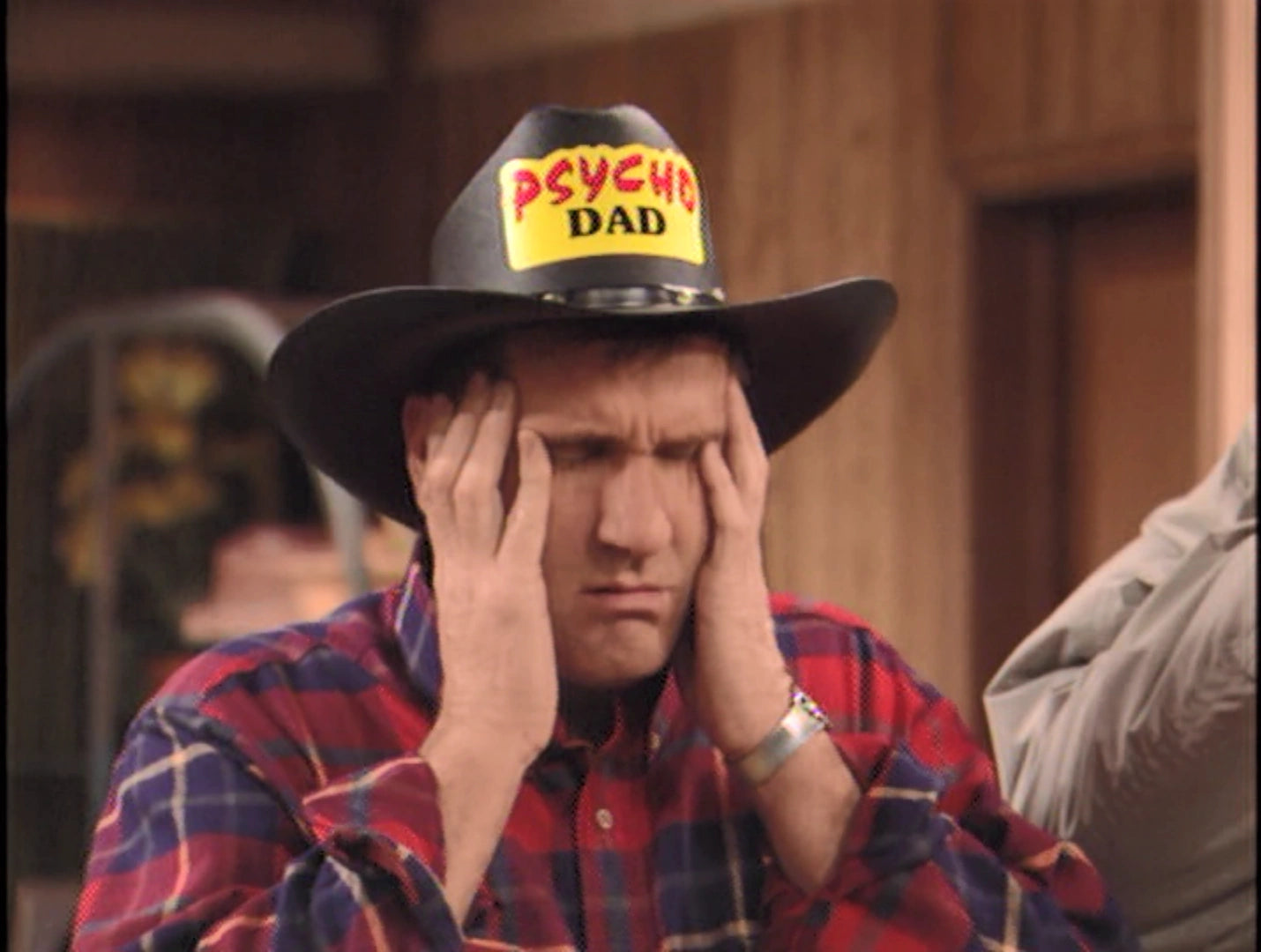 A man wearing a cowboy hat with the word "PSYCHED" printed on it, with his hands on his face, appears to be in a room with wooden walls.