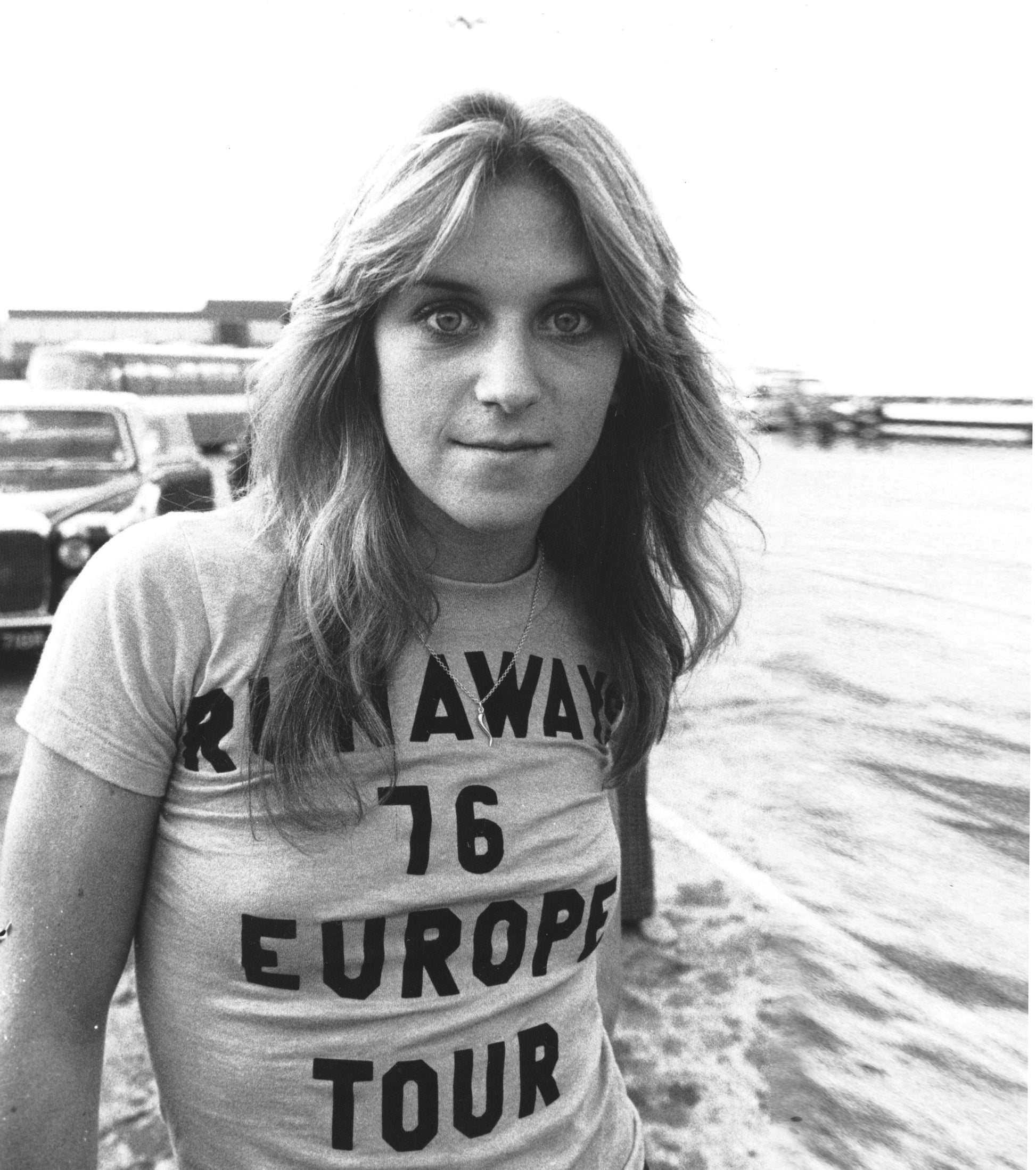 A black and white photograph of a young woman wearing a t-shirt with the text "R.I.A.W.E. 76 EUROPE TOUR" printed on it.