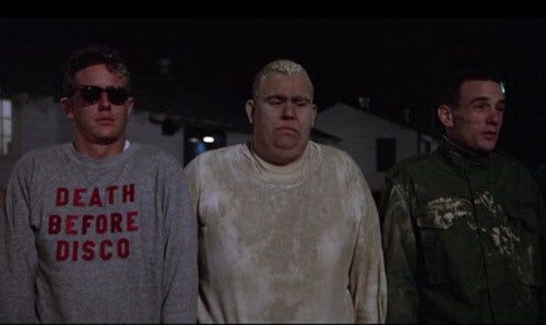 three men standing together, with one wearing a gray sweatshirt with the text "DEATH BEFORE DECCO" printed on it.