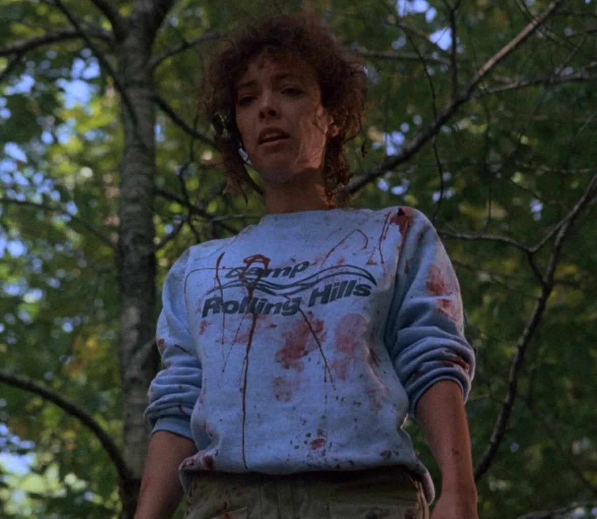 Angela from the movie Sleepaway Camp 2 wearing a bloody 'Camp Rolling Hills' sweatshirt.