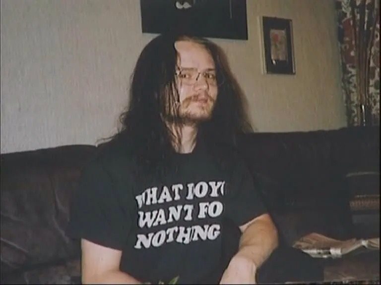 a man with long hair and glasses sitting on a couch