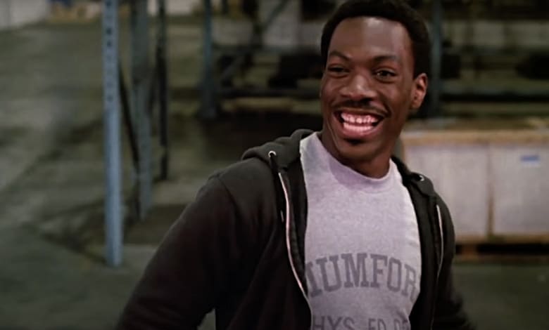 A man wearing a gray hoodie with the word "UMFORD" on it is smiling and looking to the side.