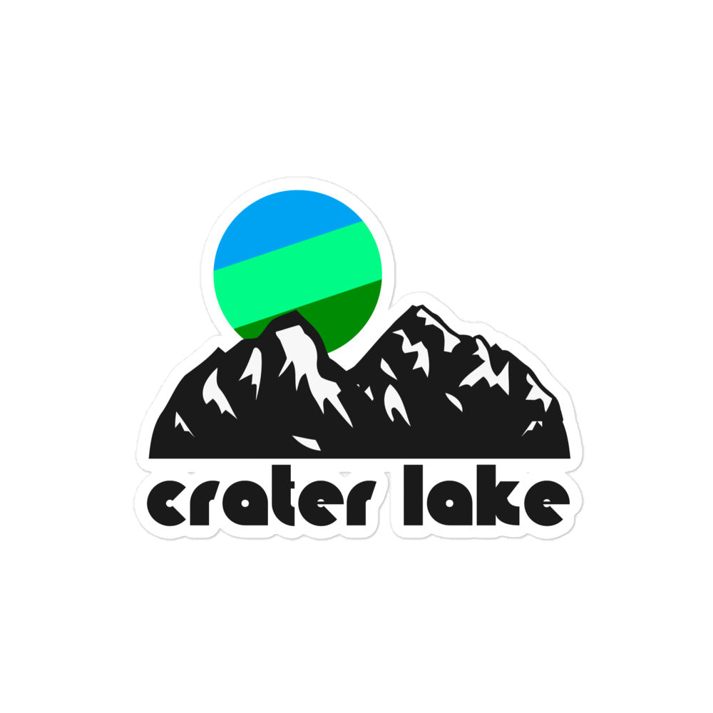 A vintage Crater Lake kiss cut sticker that includes the image of multiple snow covered mountain peaks, a cool toned sun hanging in the sky in greens and blues. 