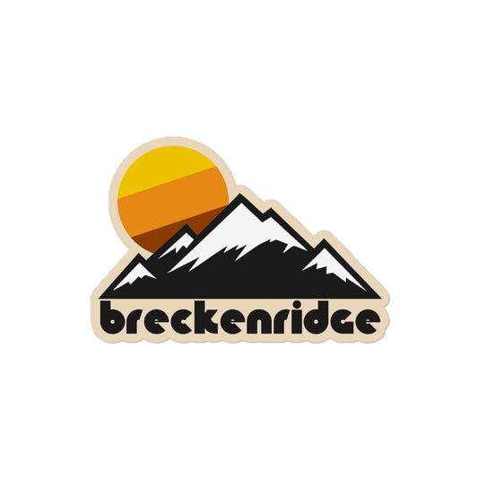 A retro kiss cut sticker that says 'Breckenridge' - a town and ski resort in CO - under the image of a mountain range with multiple snow covered peaks, representing the Ten Mile Range of the Colorado Rocky Mountains, with a tricolored warm toned yellow, orange, and brown sun setting in the distance. 