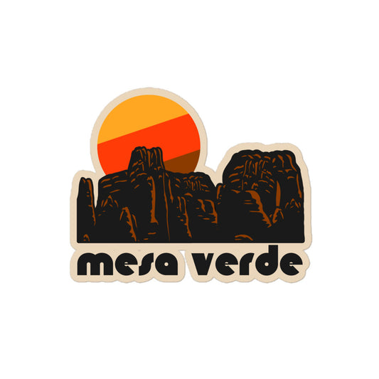 A retro kiss cut sticker that says "mesa verde" under the image of a red rock and granite landscape and a yellow, red, and brown sun, referencing Colorado's Mesa Verde National Park. 