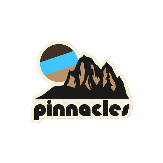 A vintage kiss cut sticker that says 'pinnacles' underneath the image of multiple brown mountain peaks and a setting tricolored sun, referencing California's Pinnacles National park, famous for being shaped by volcanic eruptions millions of years ago. 
