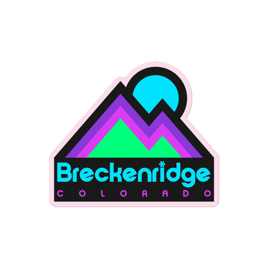 A retro Breckenridge Colorado kiss cut sticker in electric blue, purple, pink, and mint green colors. Includes image of a mountain range and rising sun in reference to the town and ski resort in the Colorado Rocky Mountains. 