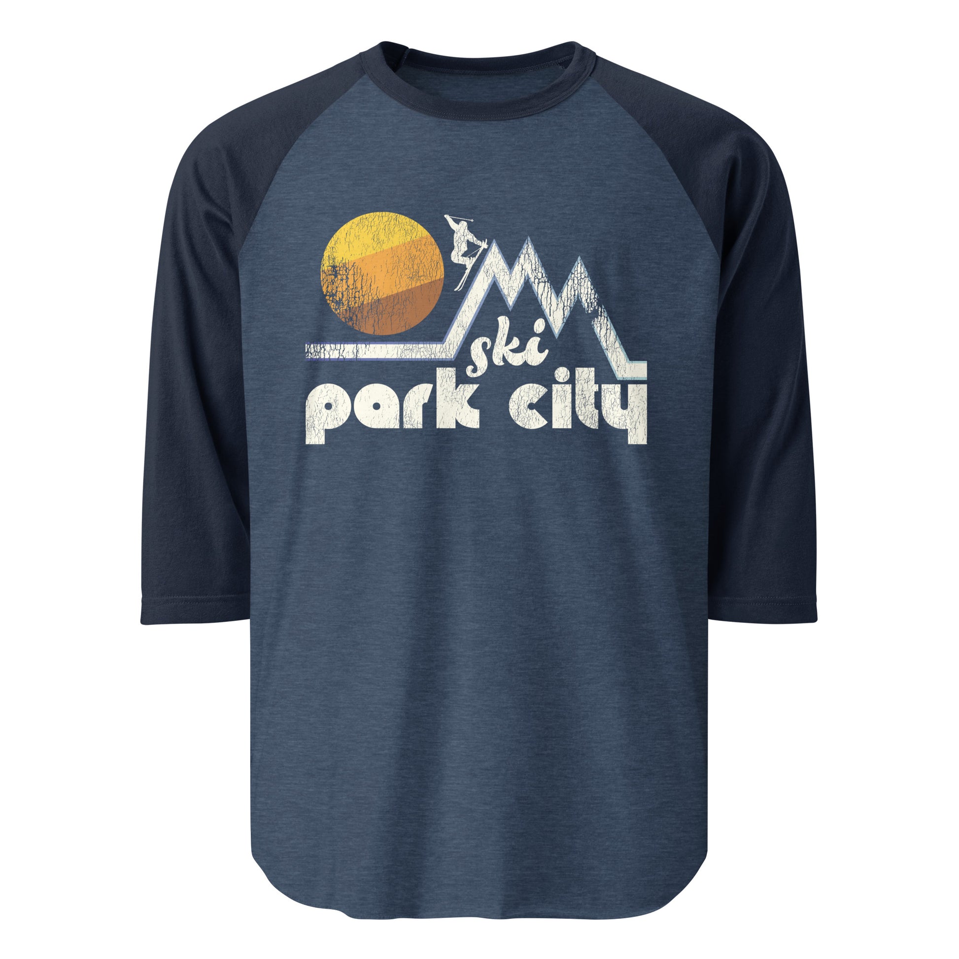 A 3/4 sleeve heather blue and navy colored raglan shirt that says "Ski Park City", referencing the famous skiing town in Utah with Park City Mountain Resort and Deer Valley Resort. Includes image of a skier headed down one of many mountain slopes, passing by a beautiful setting sun. 