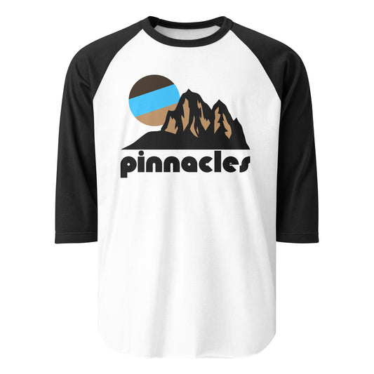 A black and white 3/4 sleeve vintage raglan style shirt that says 'pinnacles' underneath the image of a mountain landscape, a blue and brown colorful sun peaking out over the top. References Pinnacles National Park in California, famous for its pinnacles, unique rock formations, rock spires and crags, and talus caves, created by fault line action, tectonic plate movement, and volcanic eruption from millions of years ago. 