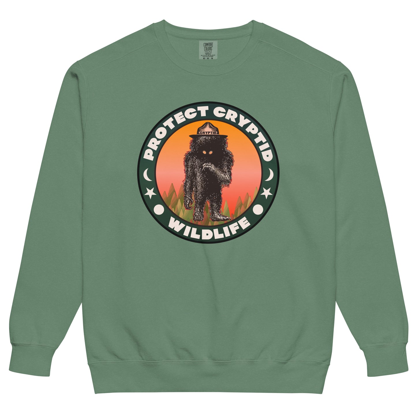 A green crew cut retro Protect Cryptid Wildlife sweatshirt. Has image of unknown beast with black fur and yellow eyes inside a forest with a pink and orange sunset. Has symbols of a sun, star, and the moon. 