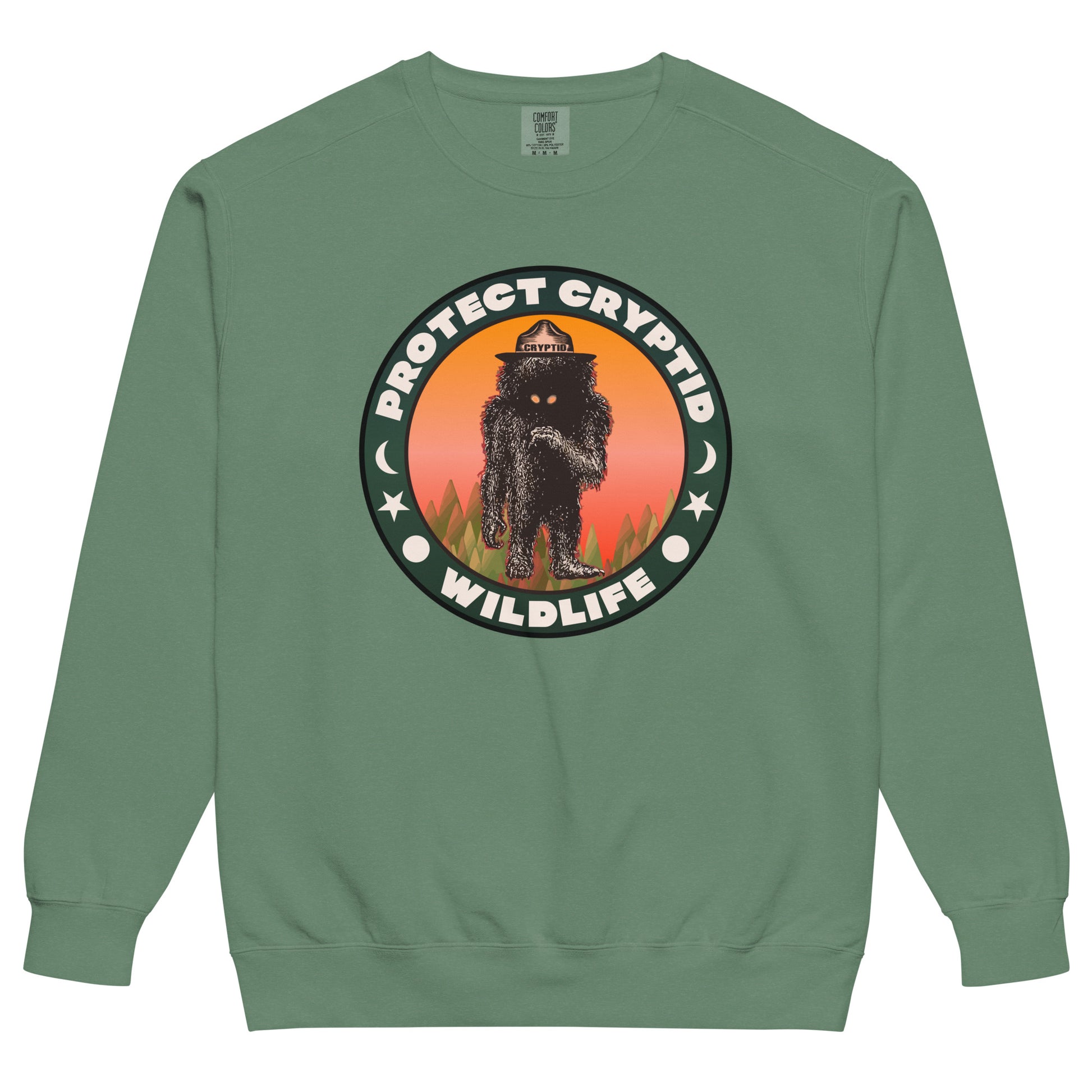 A green crew cut retro Protect Cryptid Wildlife sweatshirt. Has image of unknown beast with black fur and yellow eyes inside a forest with a pink and orange sunset. Has symbols of a sun, star, and the moon. 