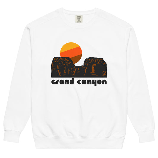 A white crew neck 80s style souvenir sweatshirt with the image of a red rock landscape, a yellow, orange, and brown sun setting in the distance. The sweatshirt says 'Grand Canyon', referencing the world famous national park, a perfect destination for tourists and adventurers, with opportunities to raft on the Colorado River, ride on mules, hiking trails down the canyon, and stunning viewpoints. 