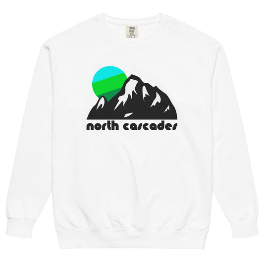 A crew neck souvenir, white colored sweatshirt with the words 'north cascades' - in reference to Washington State's North Cascades National Park and North Cascades Range - with an image of multiple tall, stunning mountain peaks and snow on the sides and a tricolored cool toned sun setting in the distance. 