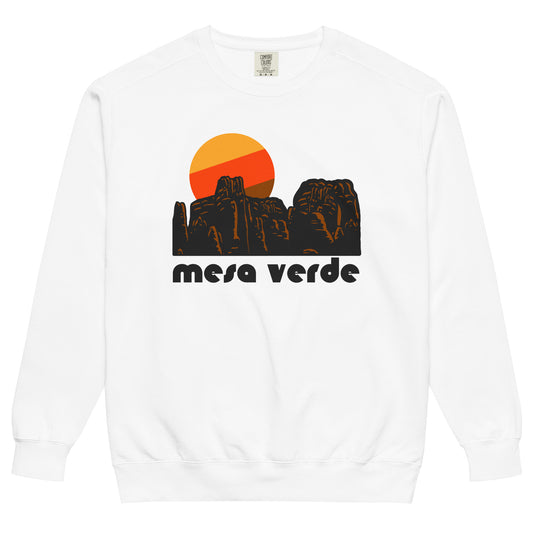 A vintage, 80s style white crew neck sweatshirt that says 'mesa verde' in reference to Mesa Verde National Park in Colorado, known for its cliff dwellings and mesa top sites of the Ancestral Pueblo peoples and culture. The sweatshirt includes an image of a red, granite, rocky landscape and a setting yellow, red, and brown sun. 