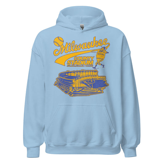 A baby blue retro tourist Milwaukee County Stadium hoodie sweatshirt with an image of an MLB player wearing a gold and blue "Brew Crew" jersey hitting a baseball with a bat over the baseball diamond and stadium. The sweatshirt says "Milwaukee, Wisconsin" and "Est. 1953". 
