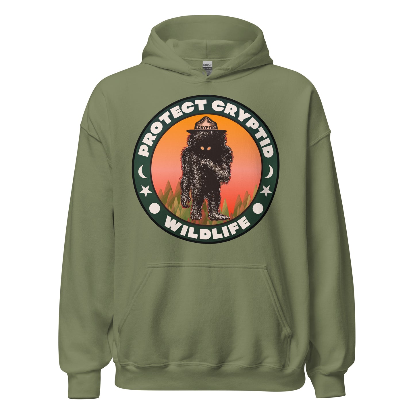 A military green retro Protect Cryptid Wildlife hoodie sweatshirt with the image of an undiscovered beast, a black and hairy creature with yellow eyes, inside trees against a pink and orange sunset. 