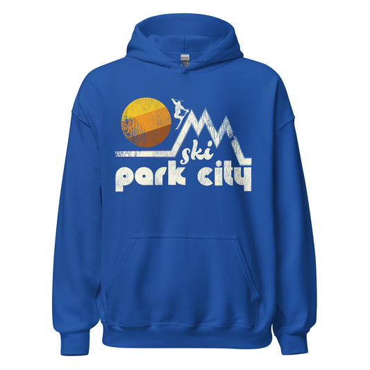 A royal blue 80s style "Ski Park City" hooded sweatshirt for tourists, from the Utah city situated in the Wasatch Mountains, known for Deer Valley Resort and Park City Mountain Resort. Image of three tall mountain peaks, a skier, and a striped warm toned sun. 