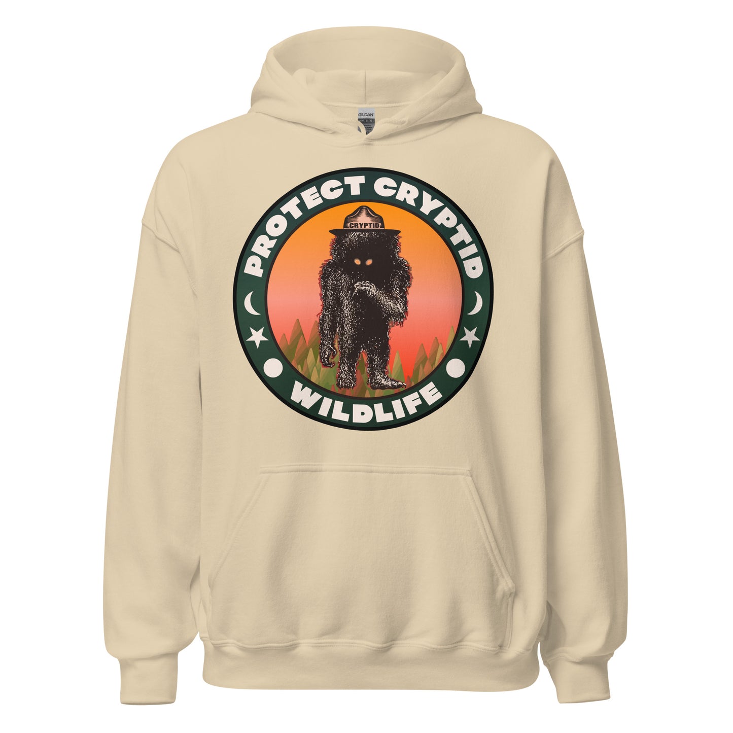 A vintage sand colored Protect Cryptid Wildlife hoodie sweatshirt with the image of an a black, hairy beast with yellow eyes, on top of a green forest against a pink and orange sunrise with a hat labeled Cryptid. 